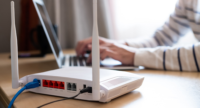 Selective focus at router. Internet router on working table with blurred man connect the cable at the background. Fast and high speed internet connection from fiber line with LAN cable connection.