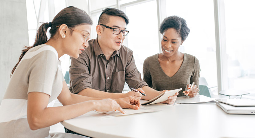 2 women and a man sitting together at a table looking over notes