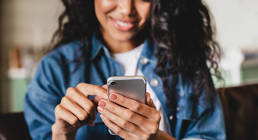 Cropped shot of young woman using smart phone at home.