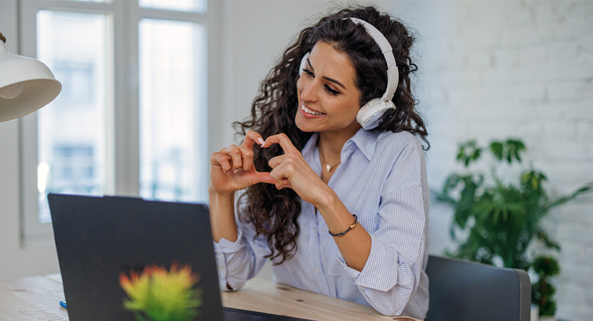 Woman making a heart with hands looking at computer